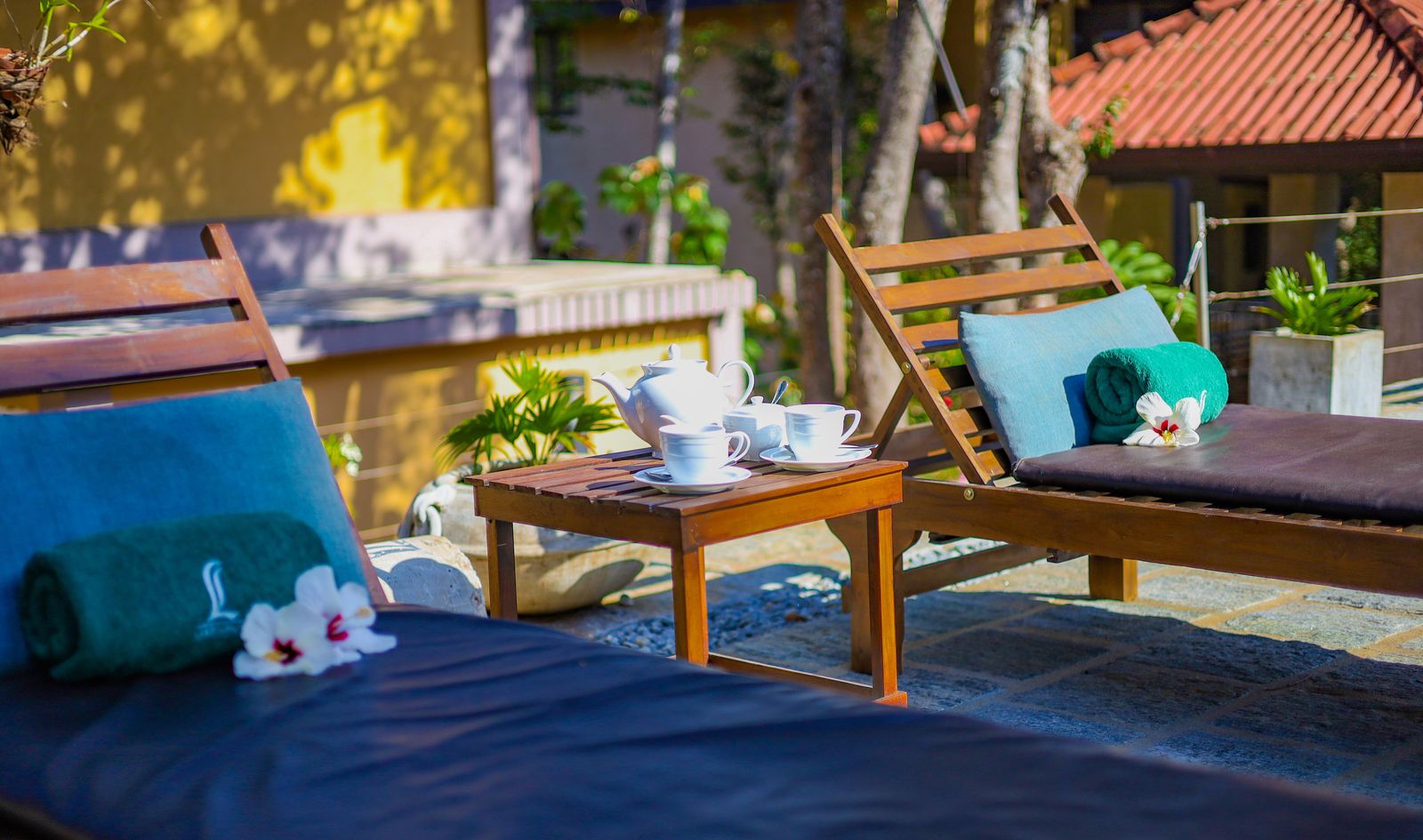 Tea for two between poolside loungers with rolled towels and frangipani flowers